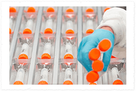 Person wearing blue gloves handling test tubes with orange caps inside the lab
